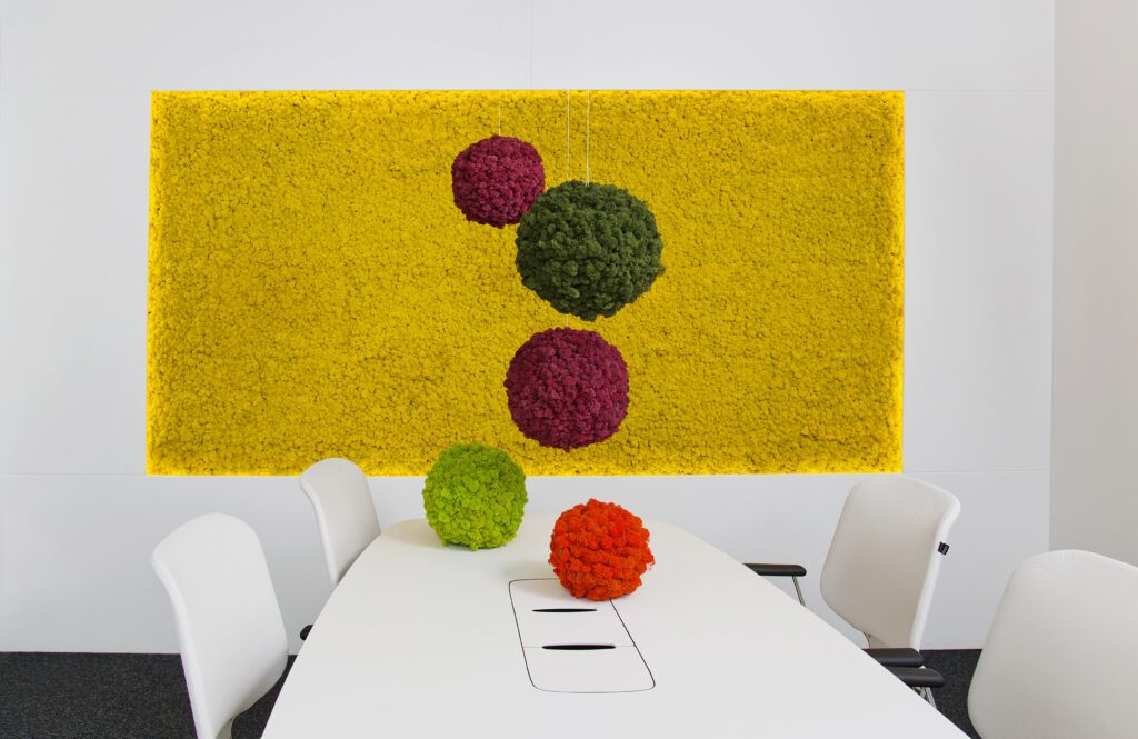 Office meeting room with several colored moss panels used for decoration. Large yellow moss panel on the wall. Green and red moss balls called Sphere hanging above the table. Moss products by Polarmoss Ltd.
